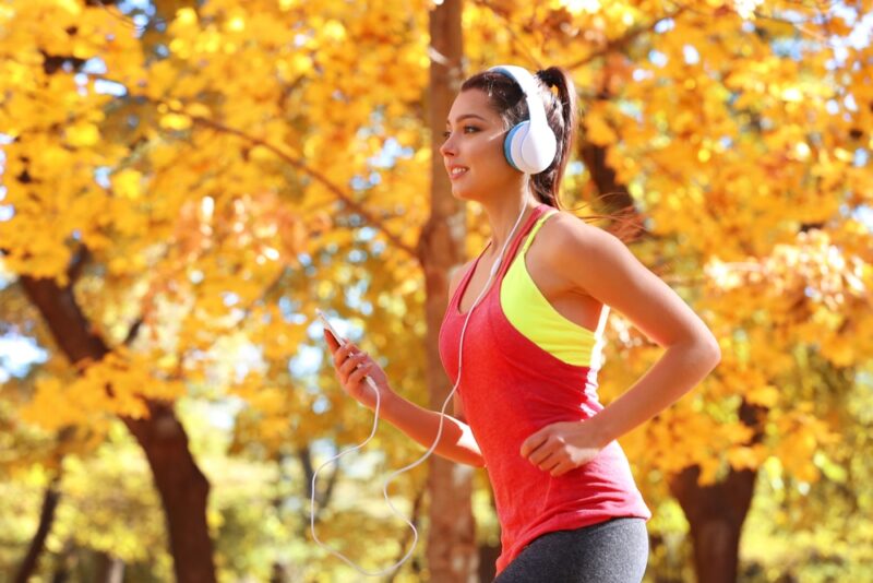 Young beautiful woman running in autumn park and listening to music with headphones