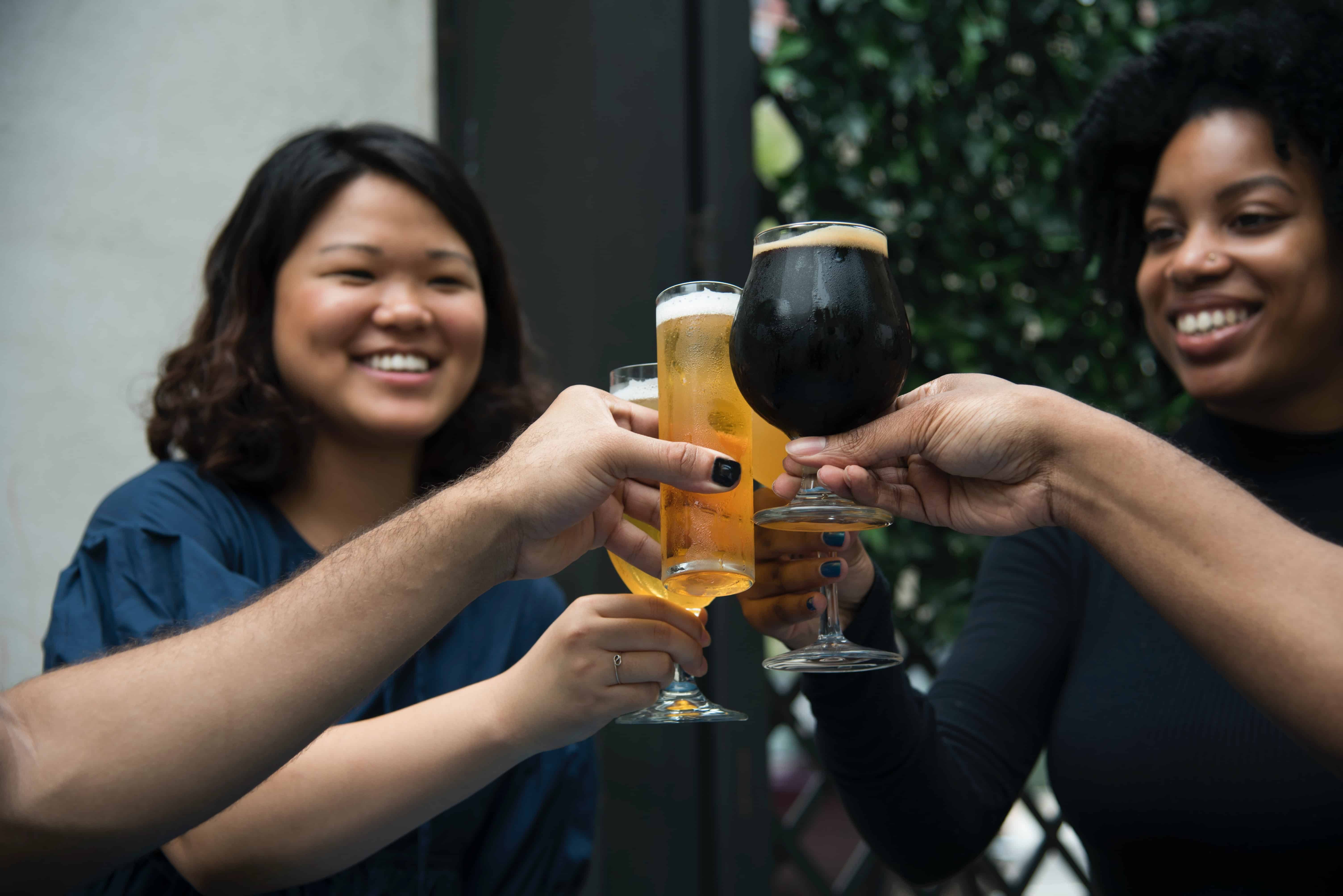 cheers with beer glasses, two women smiling in background