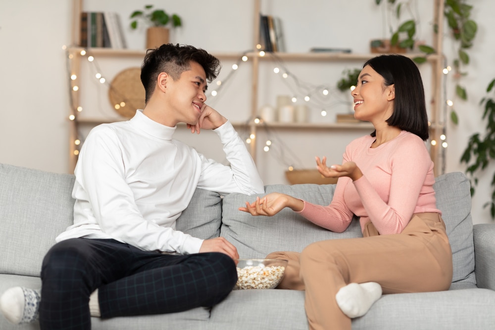 Dating-Asian-Couple-Having-Stay-At-Home-Date-Flirting-And-Talking-On-Different-Topics-Eating-Popcorn-Sitting-On-Couch-At-Home.-Weekend-Evening-Together