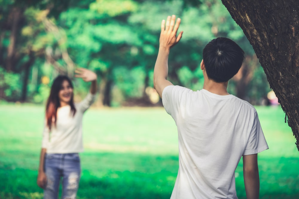Young-people-man-and-woman-greeting-or-saying-goodbye-by-waving-hands-in-the-park