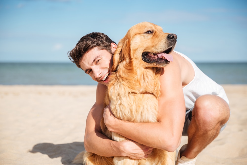 young man hugging his dog on the beach