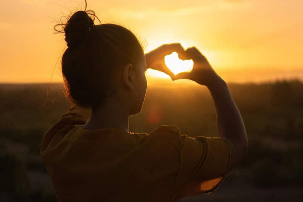 Woman Holding Hands In Heart Shape Over The Sun