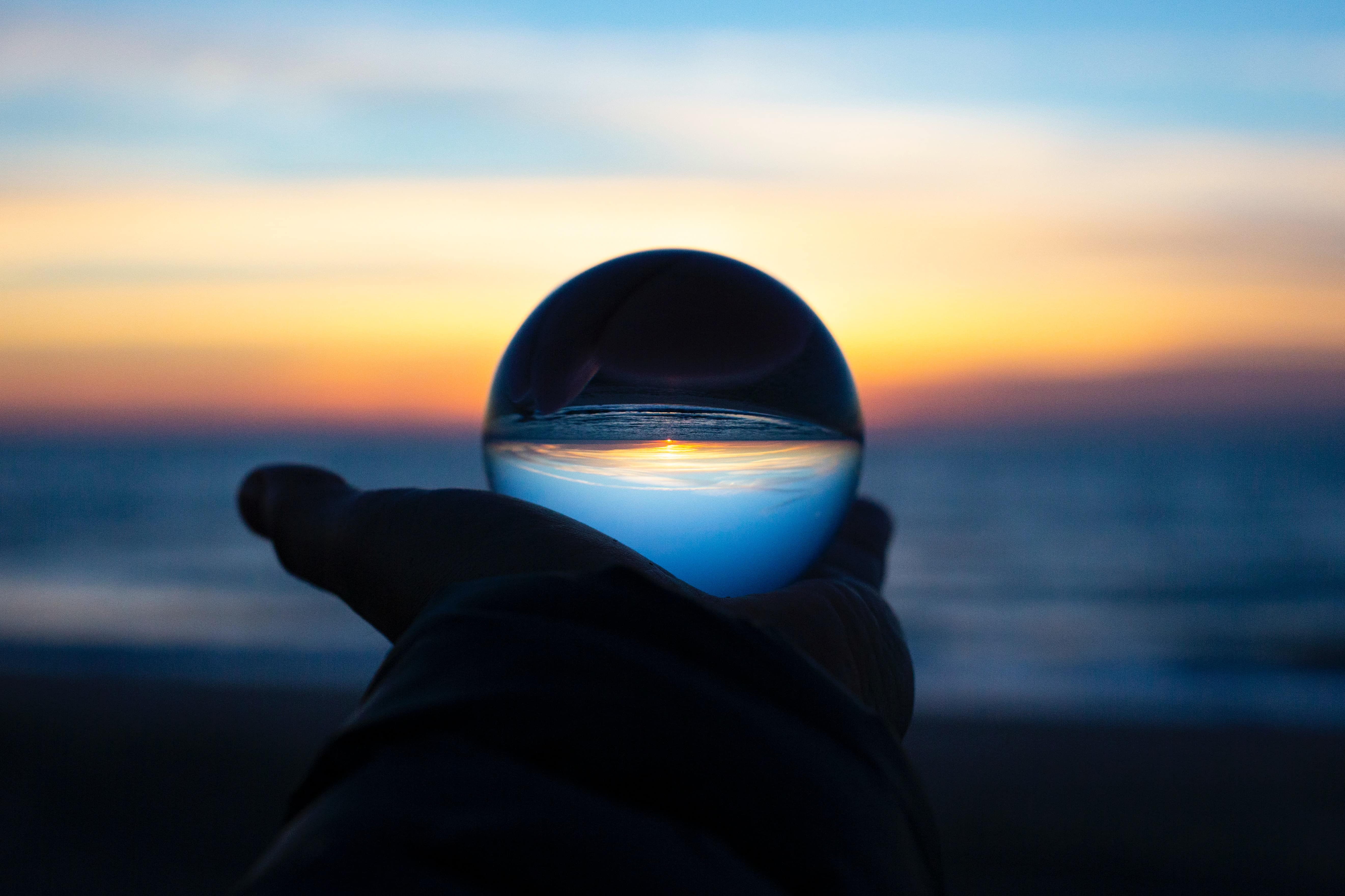 A person holds a crystal ball up in front of the sea