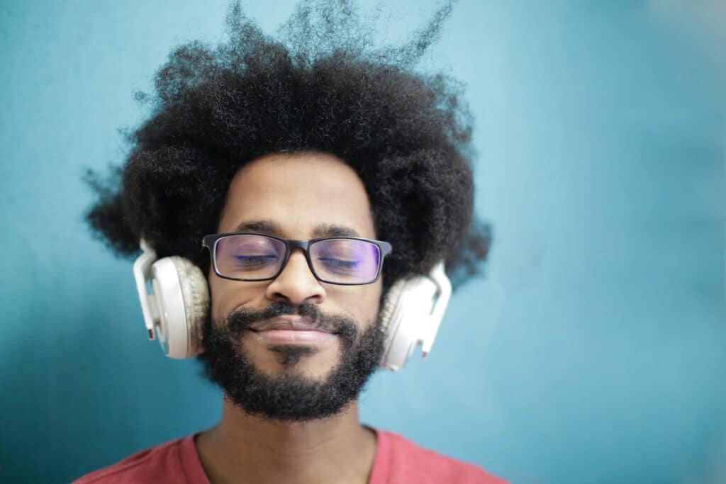 man-with-afro-and-glasses-listening-blissfully-through-white-headphones-against-blue-background