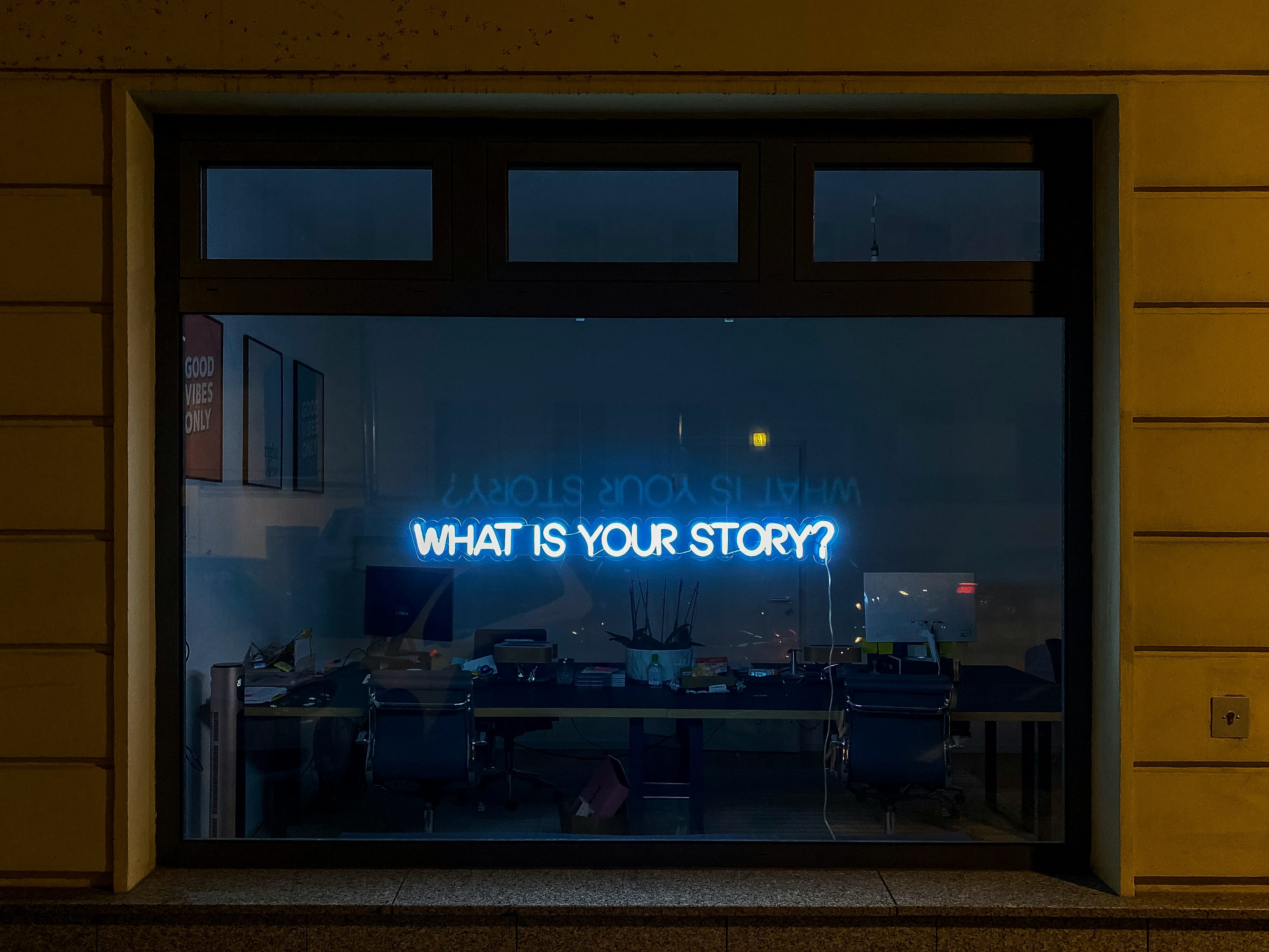 A neon sign in a window that says "what is your story?"