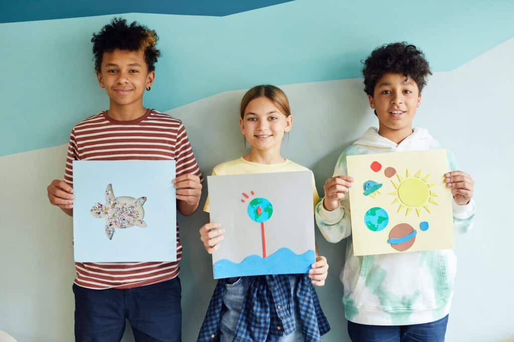three-school-children-displaying-pictures-they've-drawn