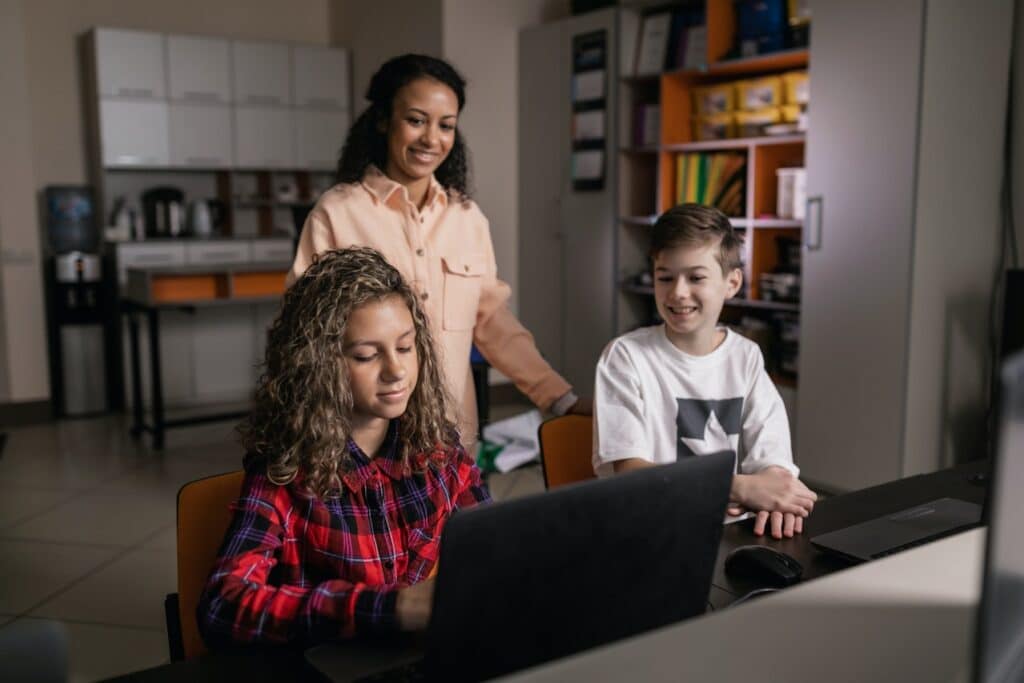 two kids using a laptop and an adult in the room