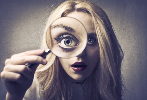 blonde woman holding magnifying glass in front of eye