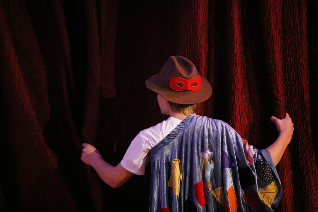 Person dressed up in a hat and cape facing a theater curtain