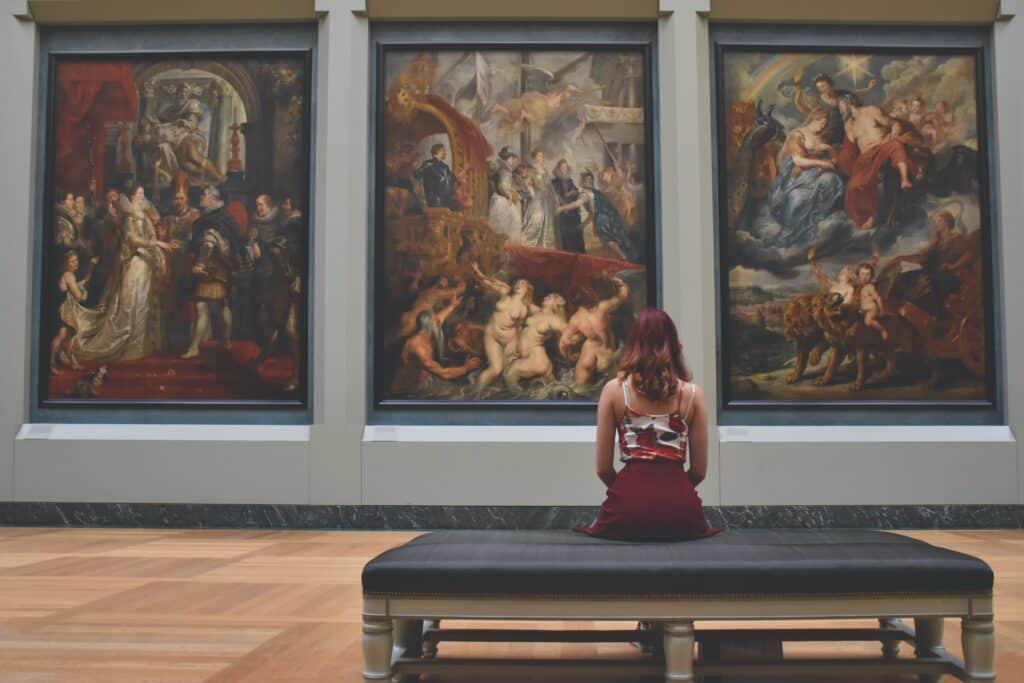 A woman sits in a museum gallery looking at a painting