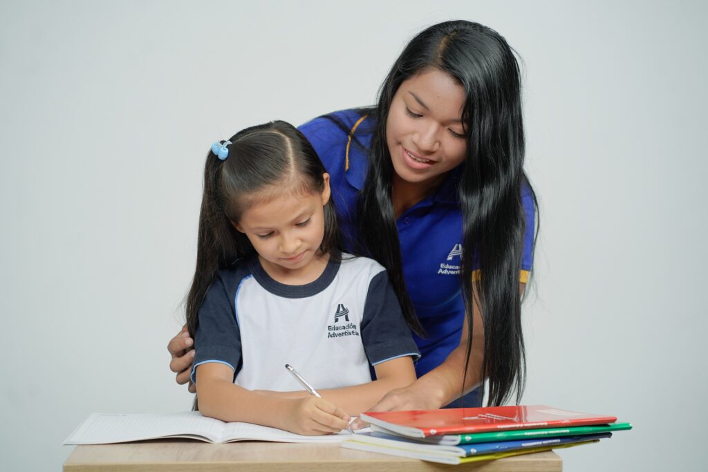 young-woman-in-blue-shirt-teaching-girl-writing-in-notebook