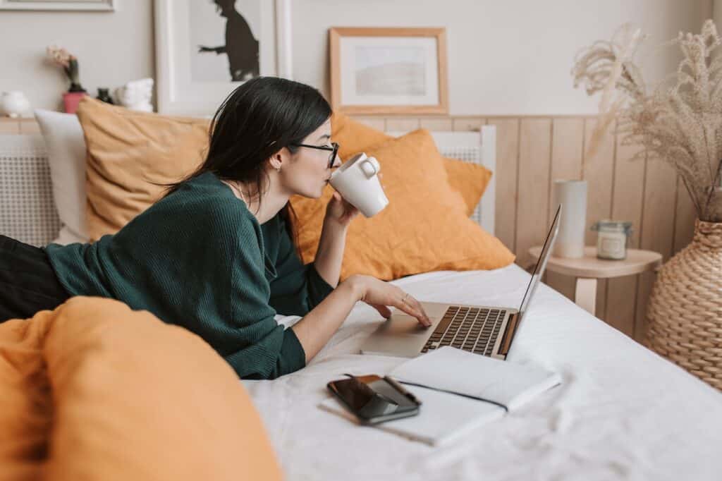 girl having a coffee and using a laptop in bed
