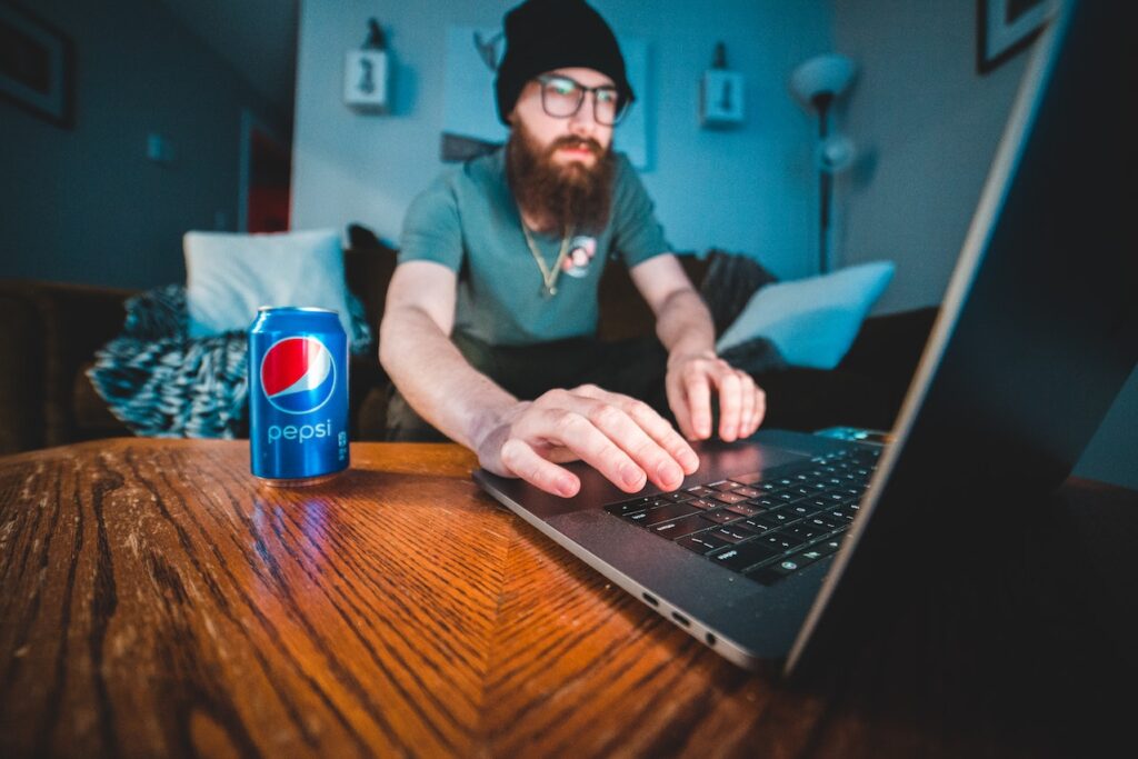 Man with a beard using a laptop and drinking Pepsi
