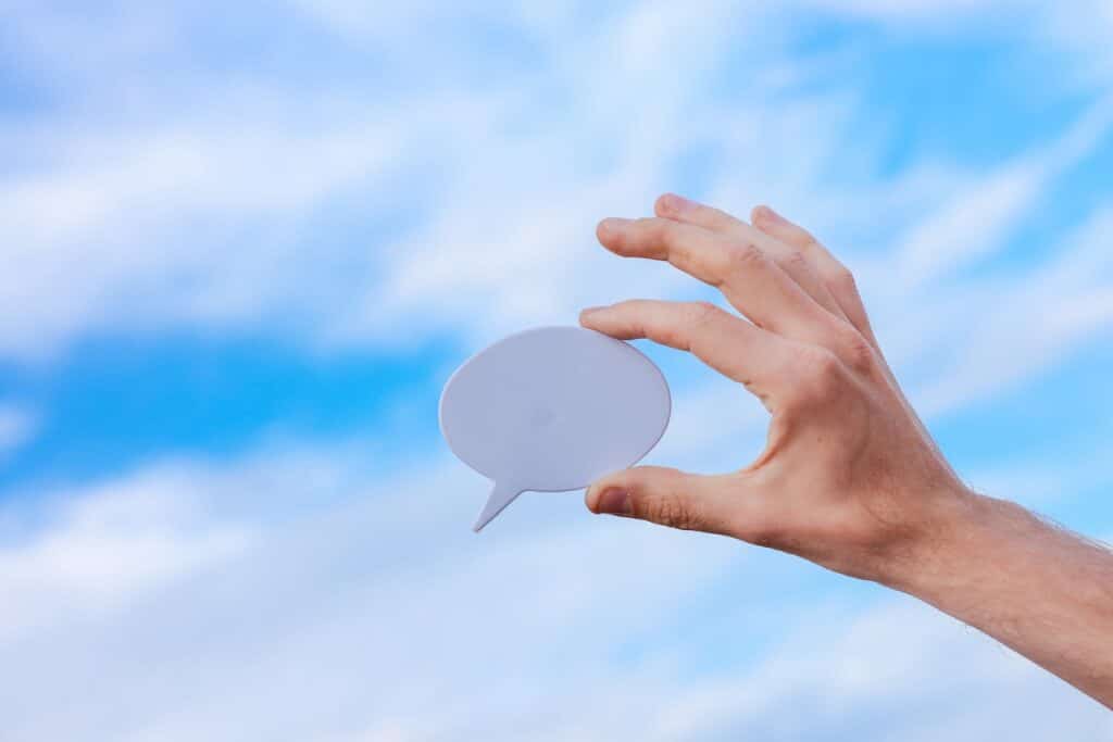 Hand holding a paper in the form of a speech bubble against a sky background.