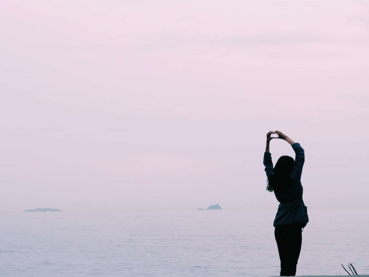 Girl in front of the sea making a hear with hands
