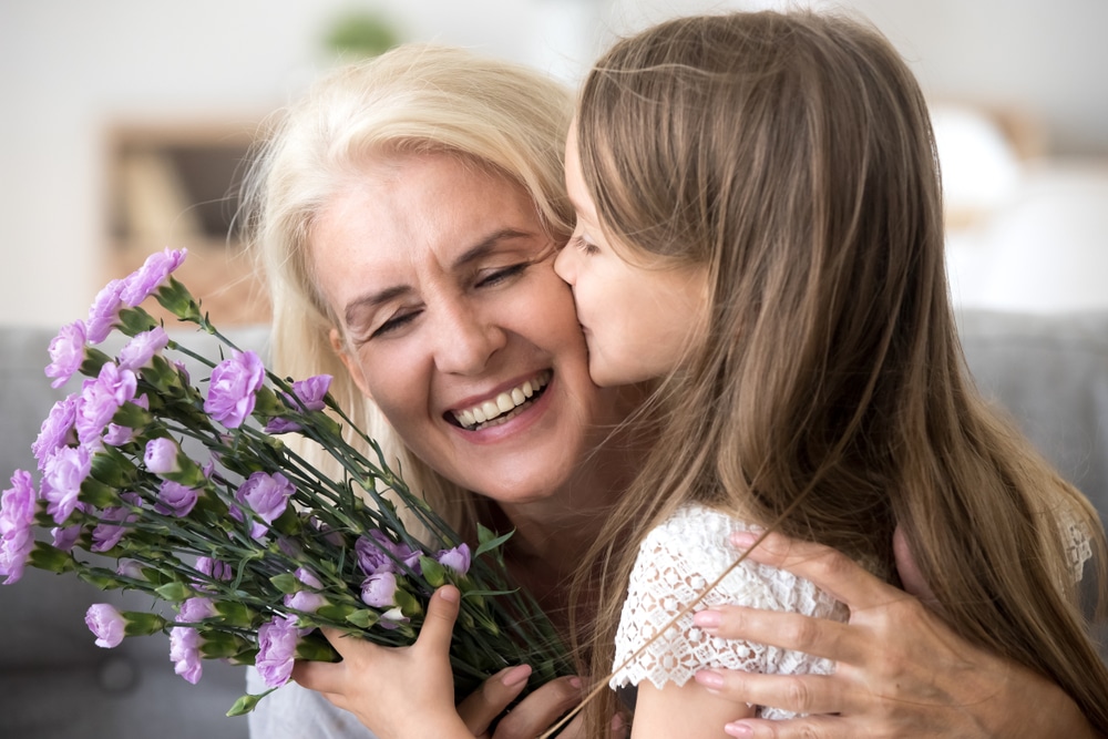 Young girl kissing her grandmother with flower in her hand