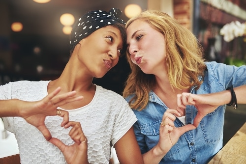 two-women-looking-at-each-other-making-a-heart-sign-with-their-hands-blowing-a-kiss