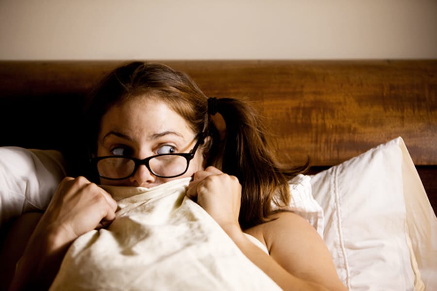Girl looking scared in bed with the covers pulled over her mouth