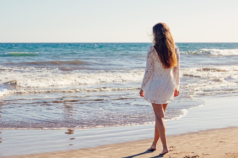 a-woman-standing-at-the-shore-on-a-beach-looking-out-at-the-sea