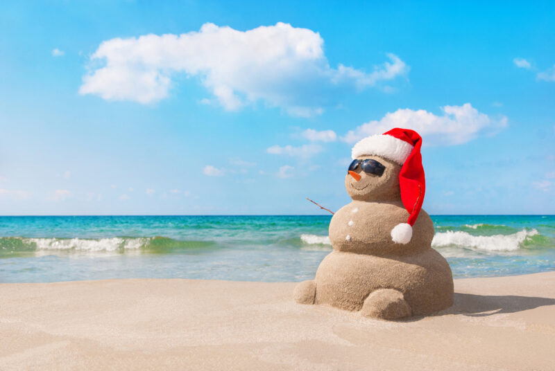 snowman-made-of-sand-on-a-beach-in-the-summer-with-a-santa-hat-and-sunglasses