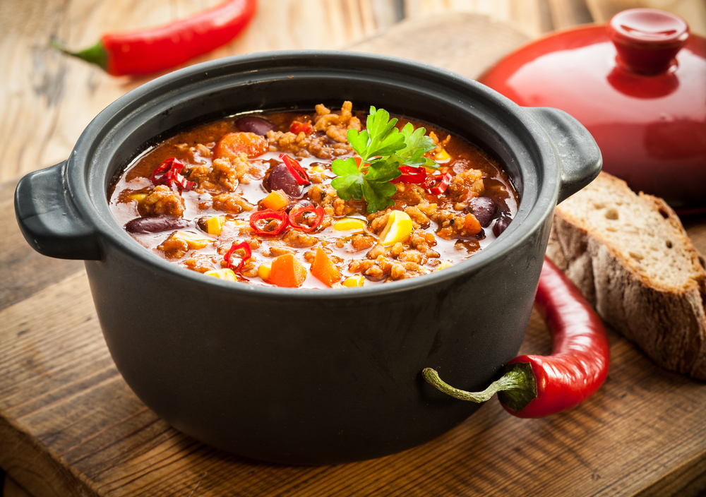A pot of stew with bread and chili peppers on a serving board
