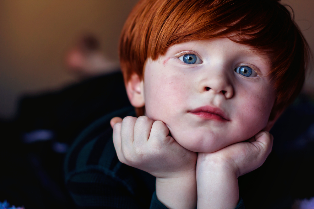 Portrait of a child with red hair and blue eyes, resting chin on hands