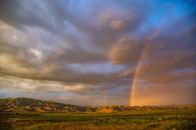 Cloudy sky with double rainbow over plains at sunset