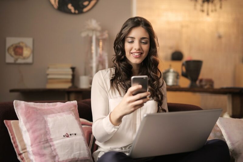 woman-on-a-couch-with-a-laptop-looking-at-her-phone