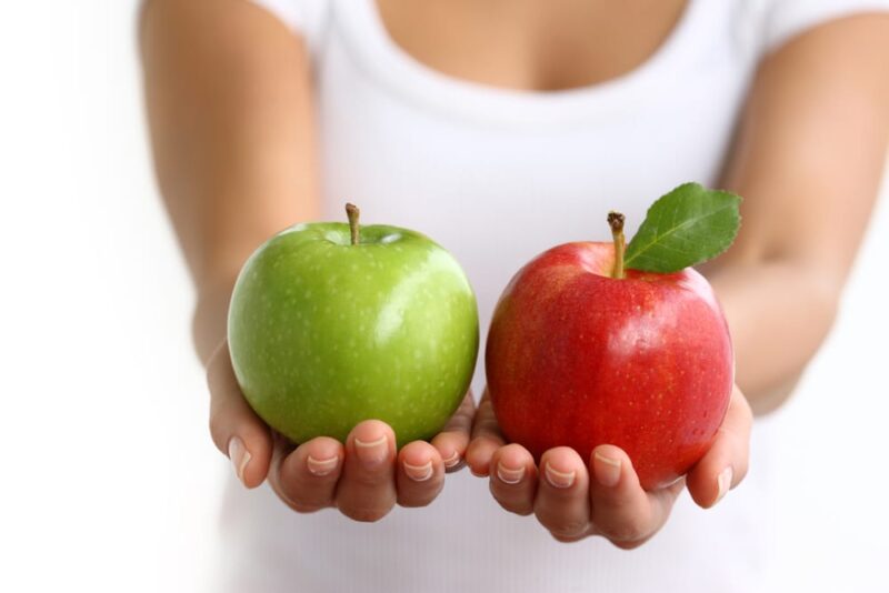 Hands holding a red and a green apple.