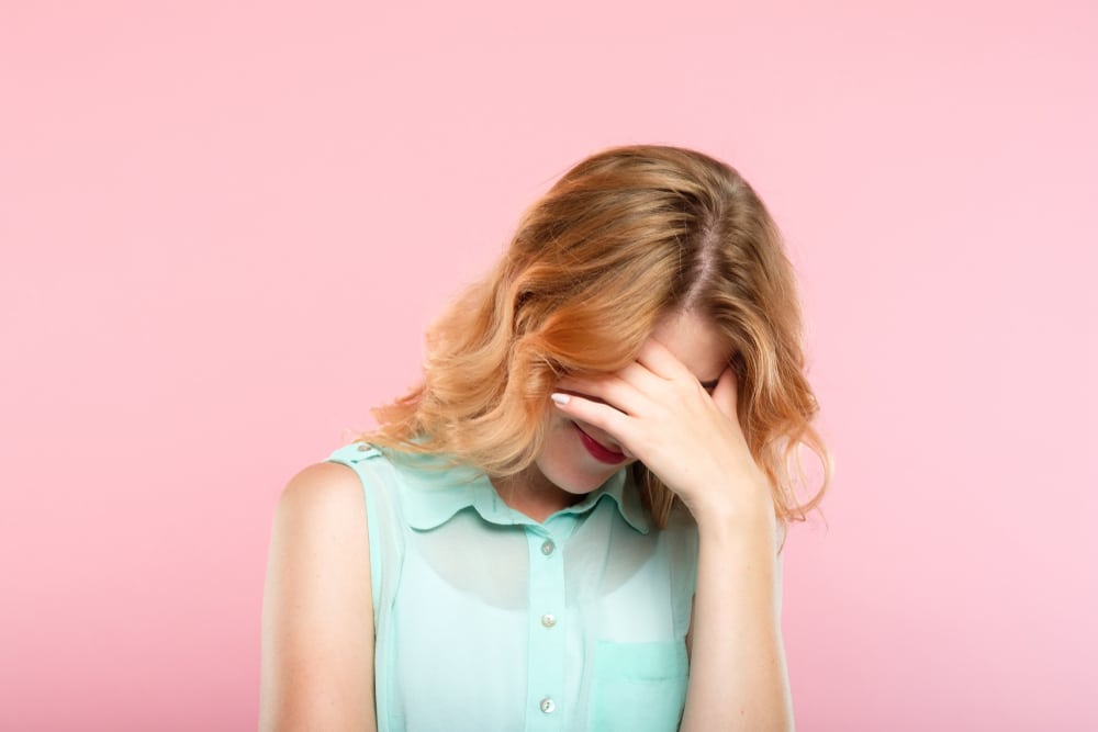 facepalm embarrassment and shame emotion ashamed woman covering her face with a hand on a pink background