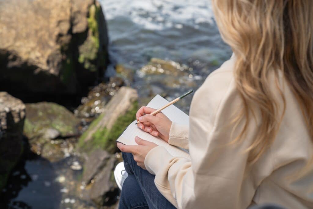 girl by river writing in notebook