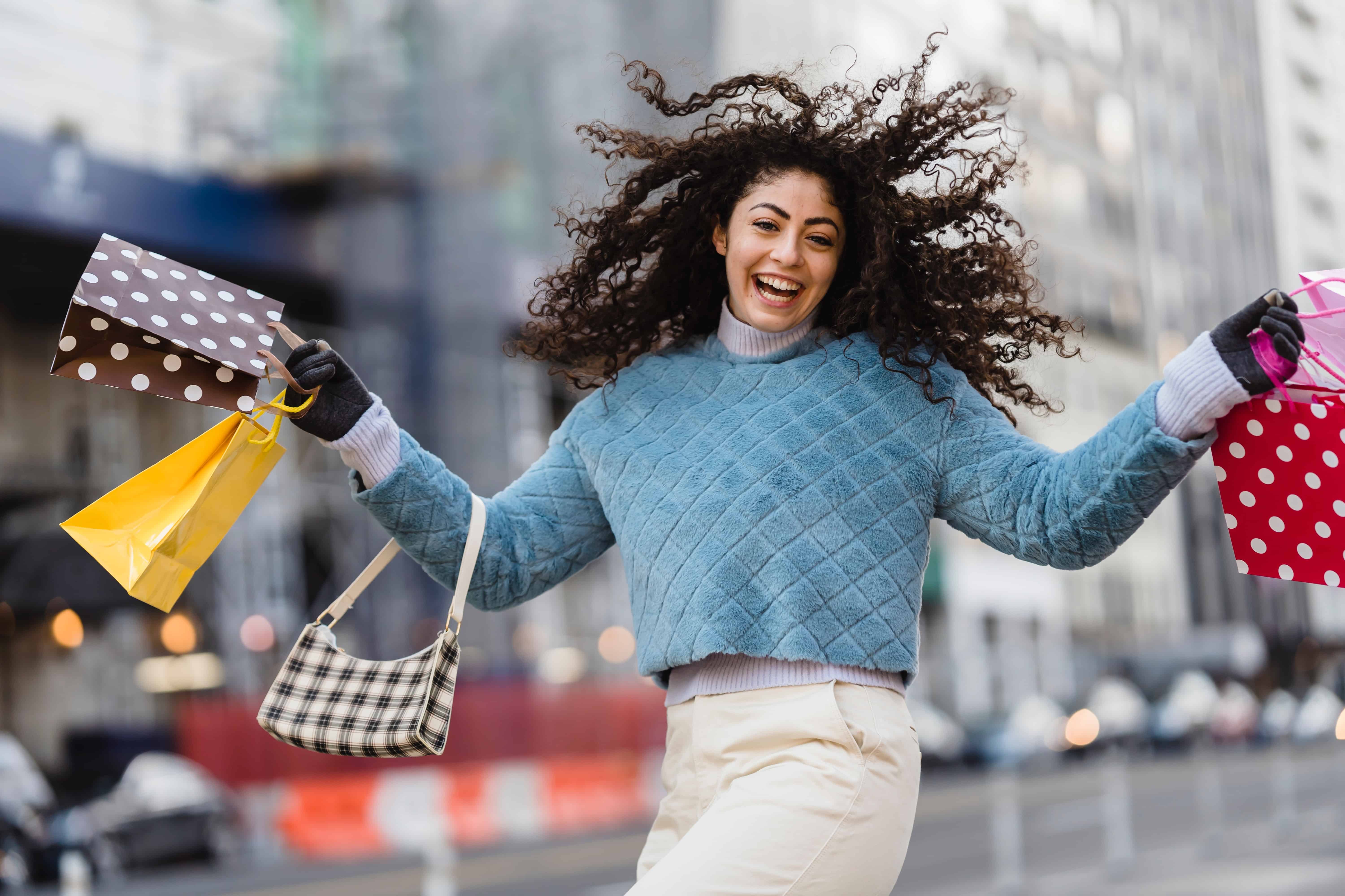 Photo by Tim Douglas : https://www.pexels.com/photo/happy-woman-jumping-with-shopping-bags-6567607/