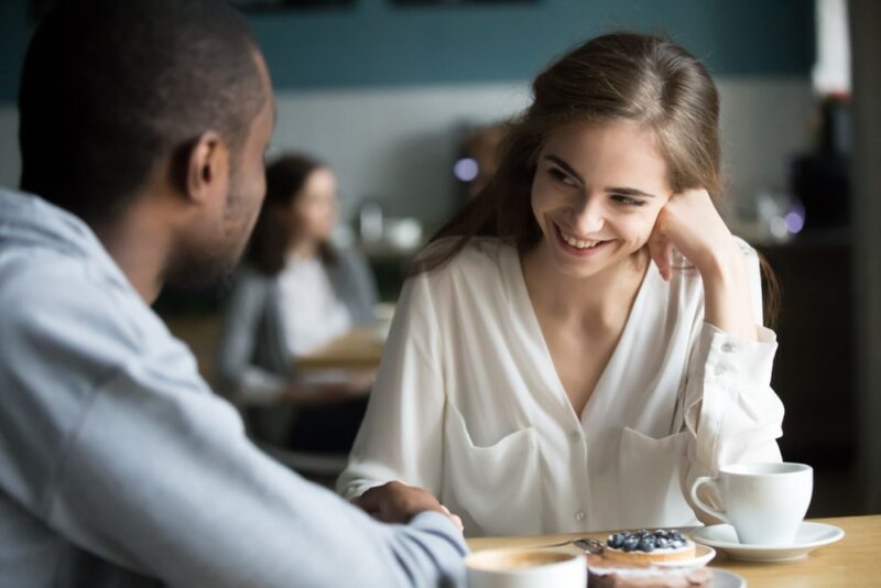 happy interracial couple flirting and talking at cafe table