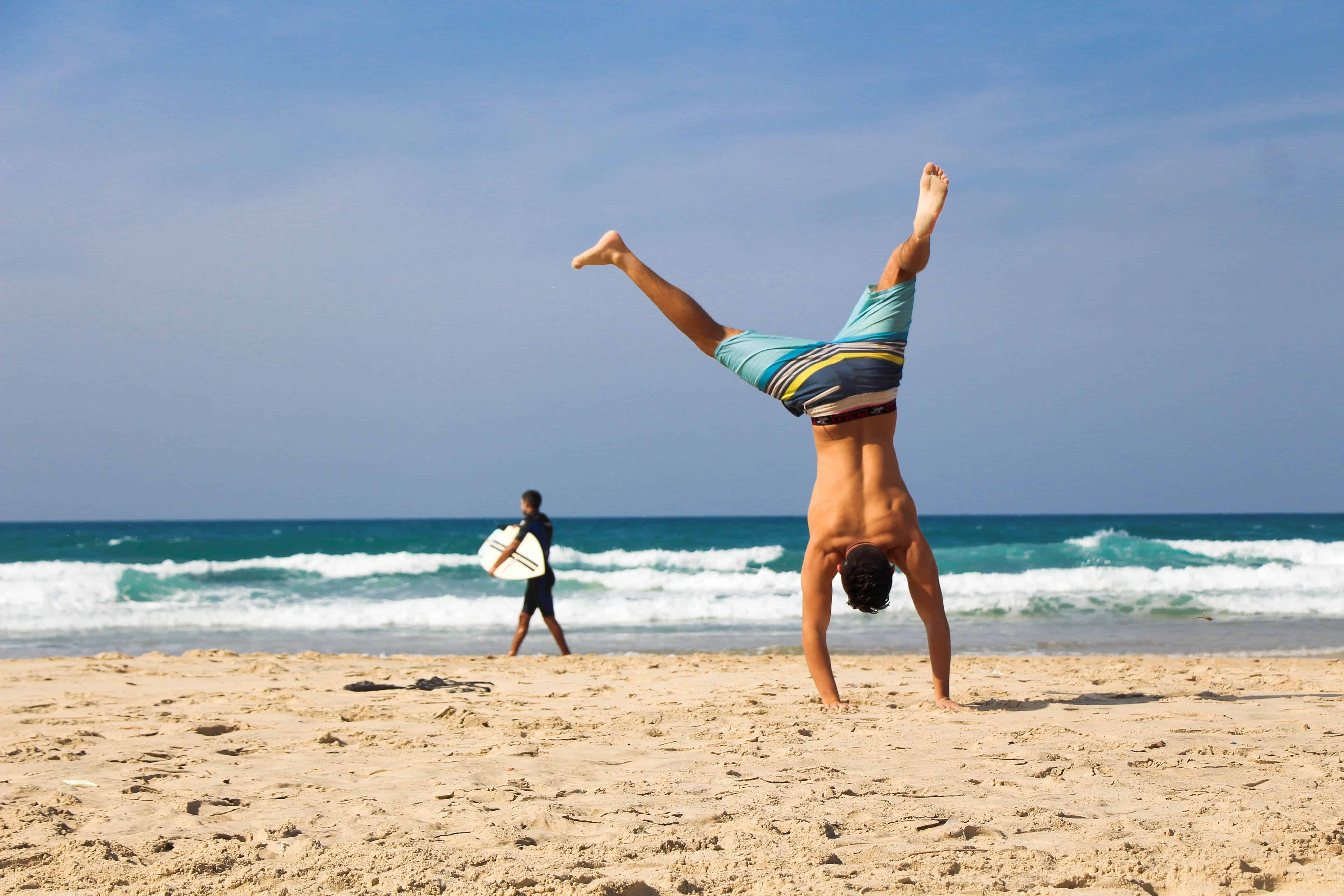 A surfer doing a handstand on the beach