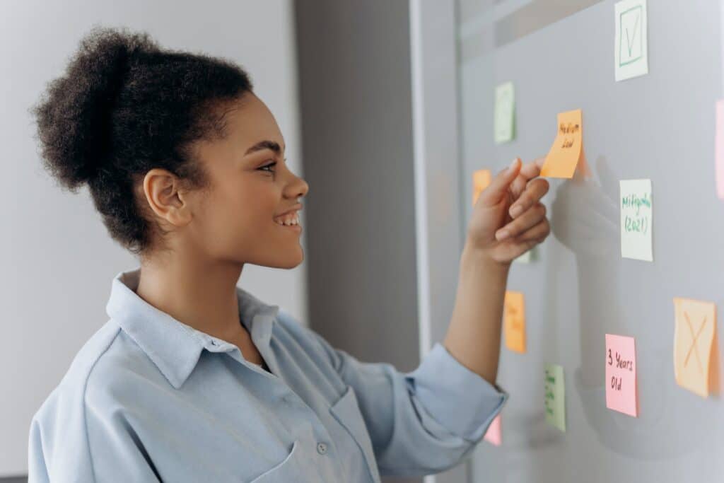 side-profile-view-of-woman-smiling-as-she-looks-at-sticky-notes-stuck-on-board