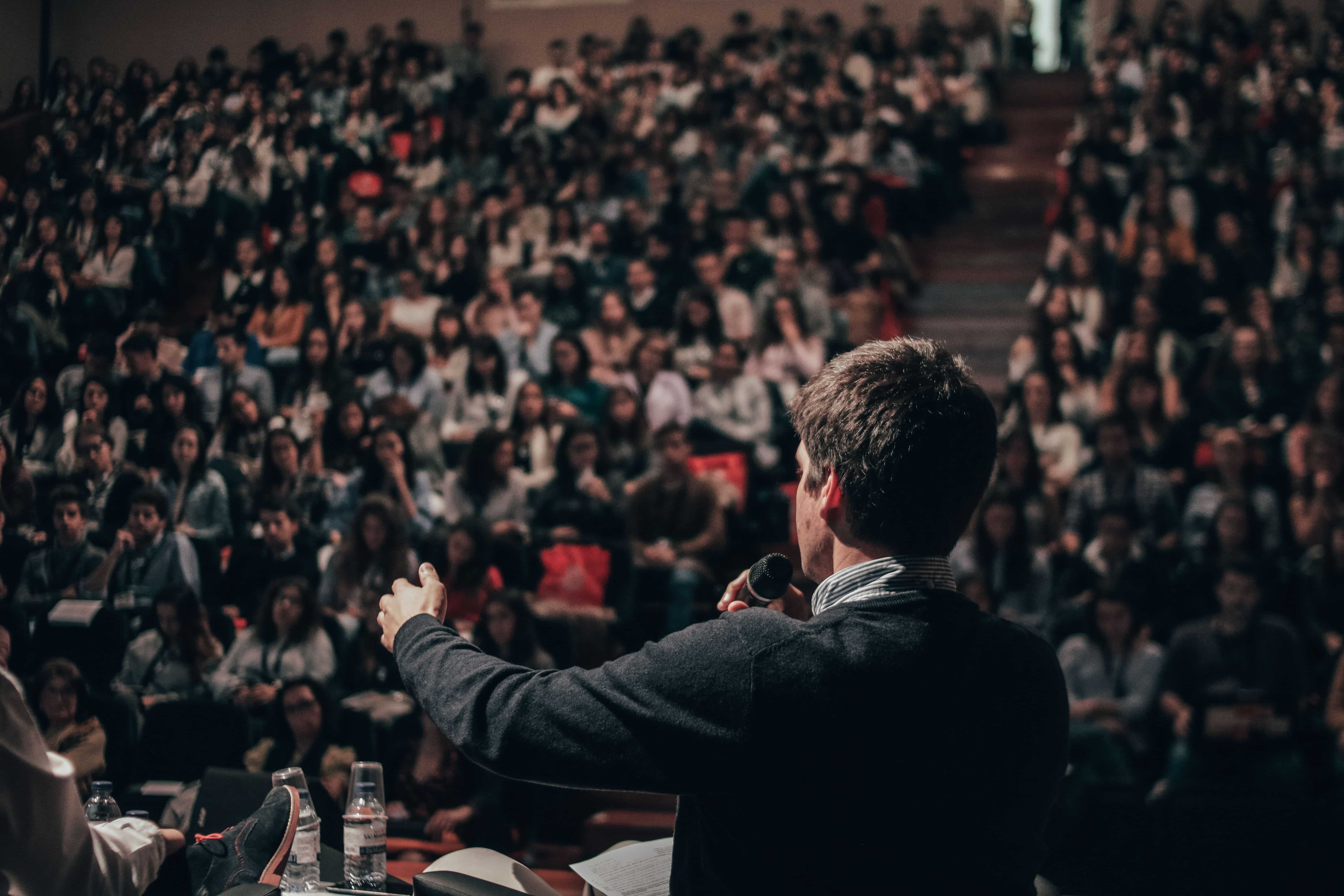 A man delivers a speech in front of a crowded auditorium