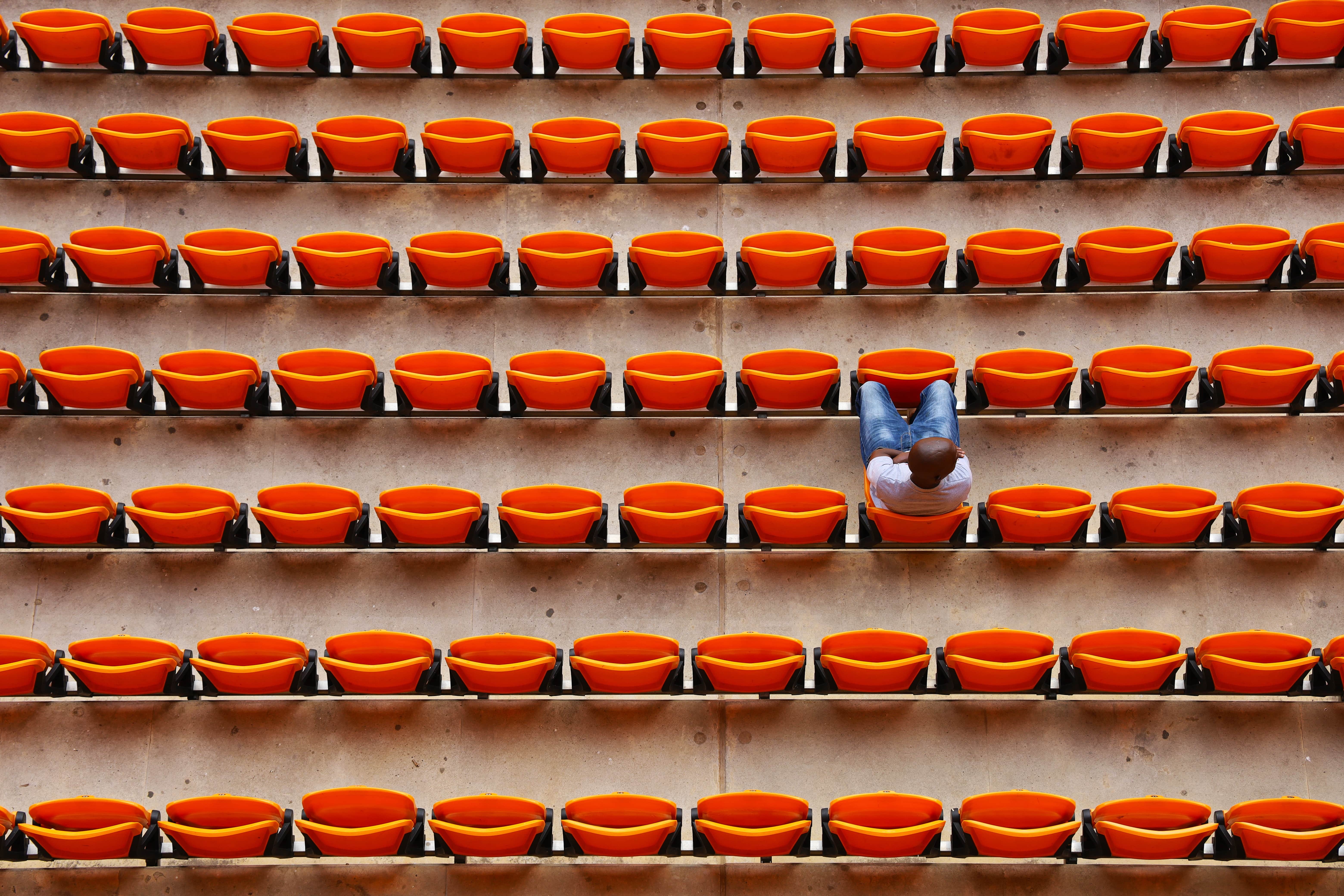 Rows of repeating orange stadium seats with one man sitting