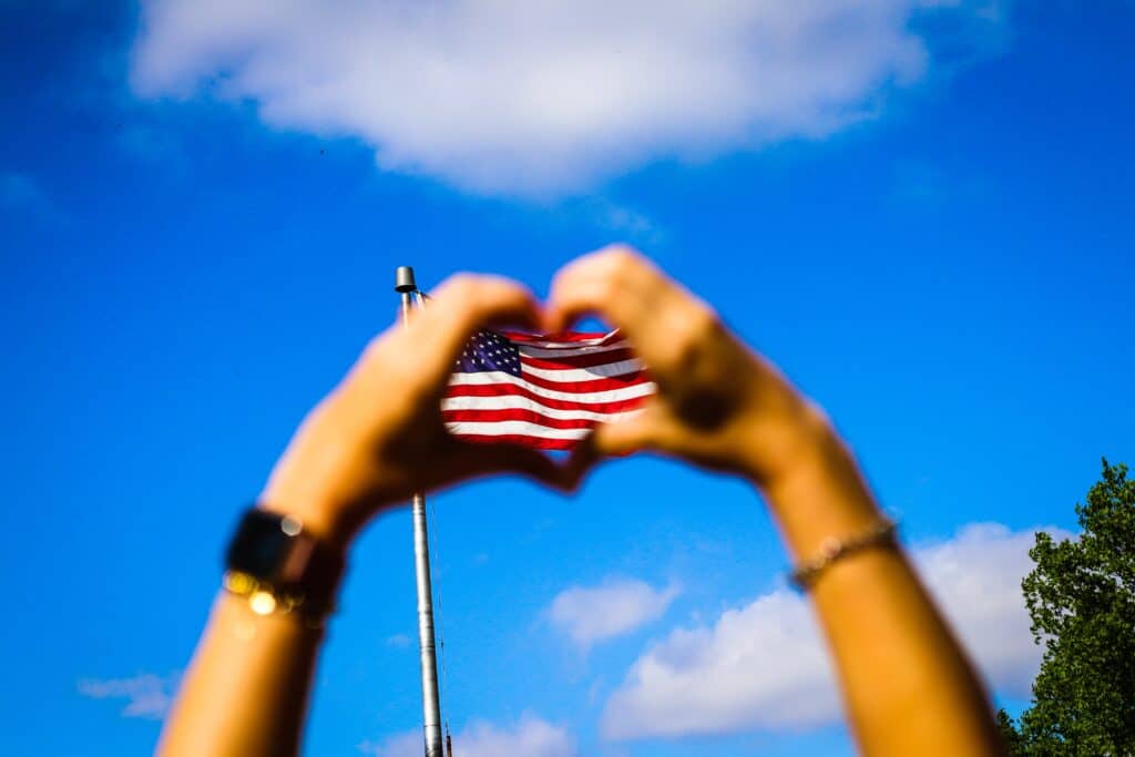 A person making a heart with their hands in front of an American flag