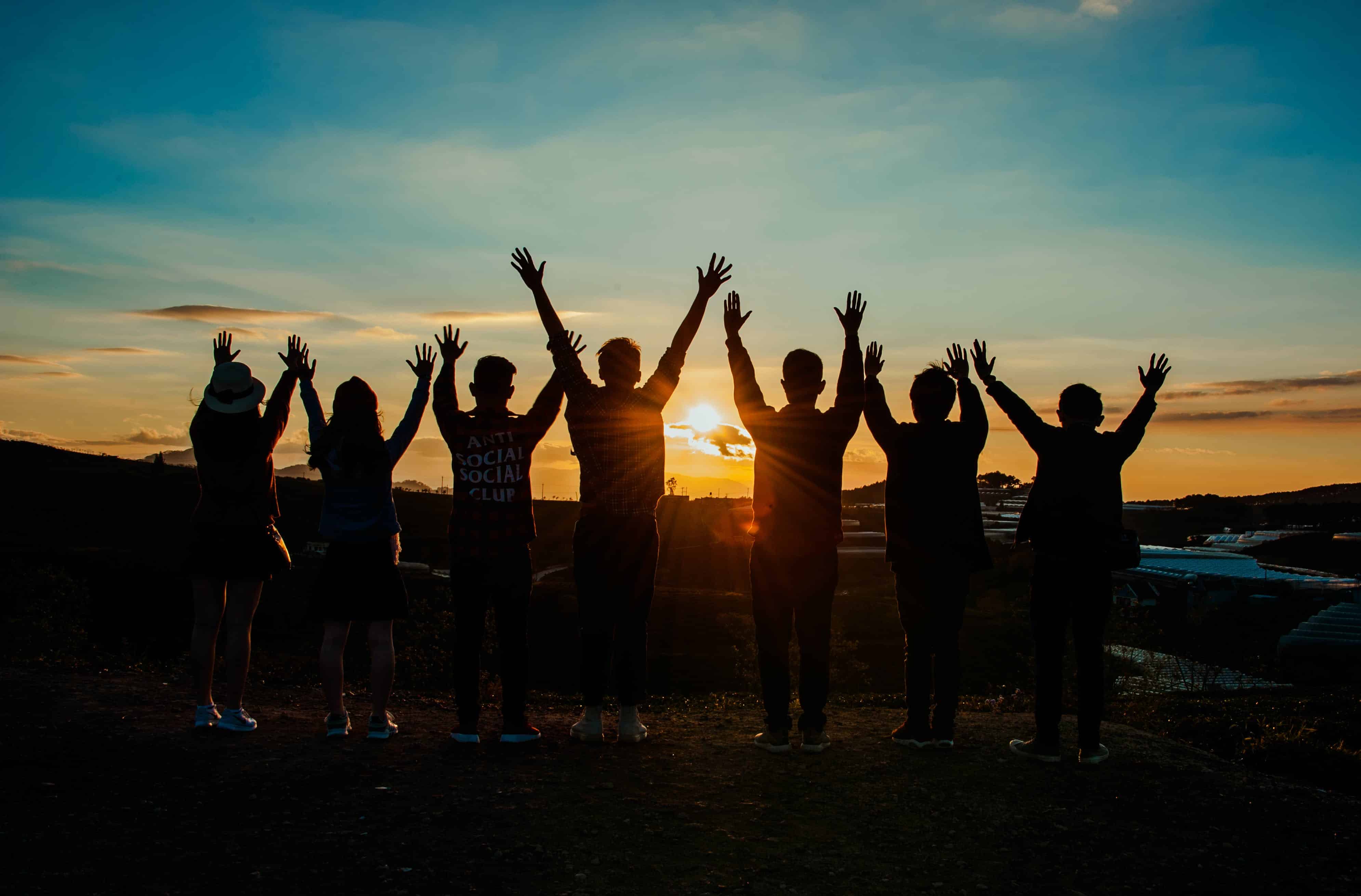 A group of friends holding their hands up at sunset on a beach