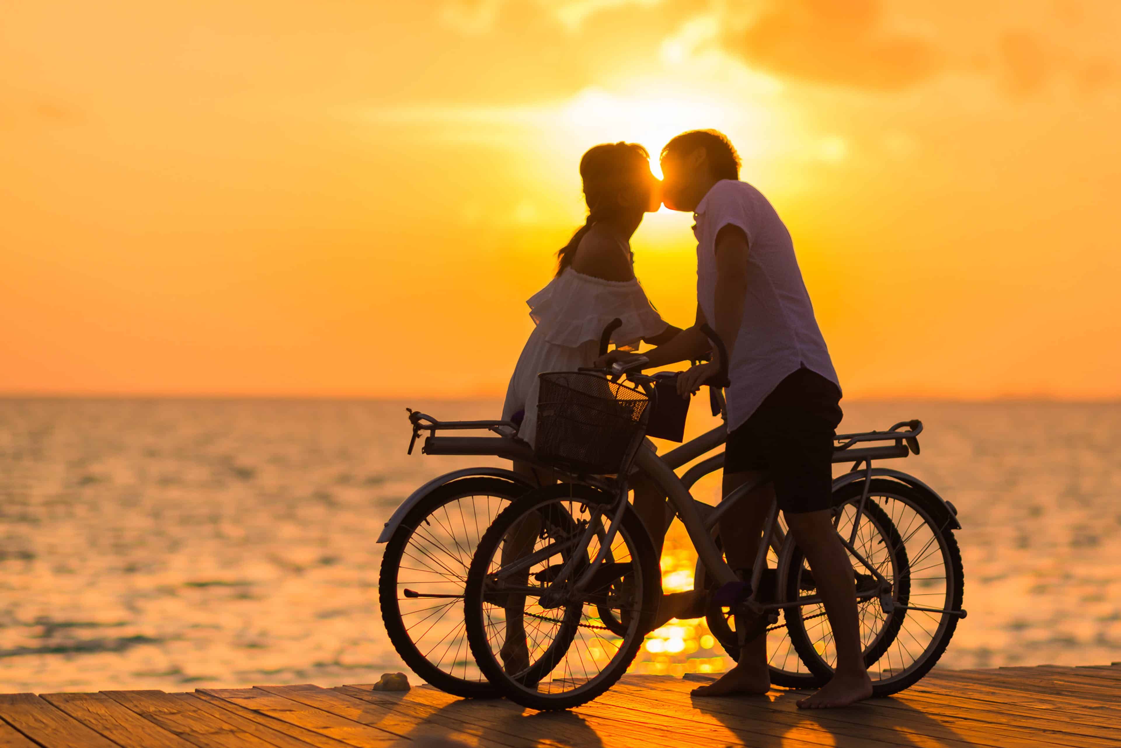 A couple stops to have a kiss while on their bicycles at sunset