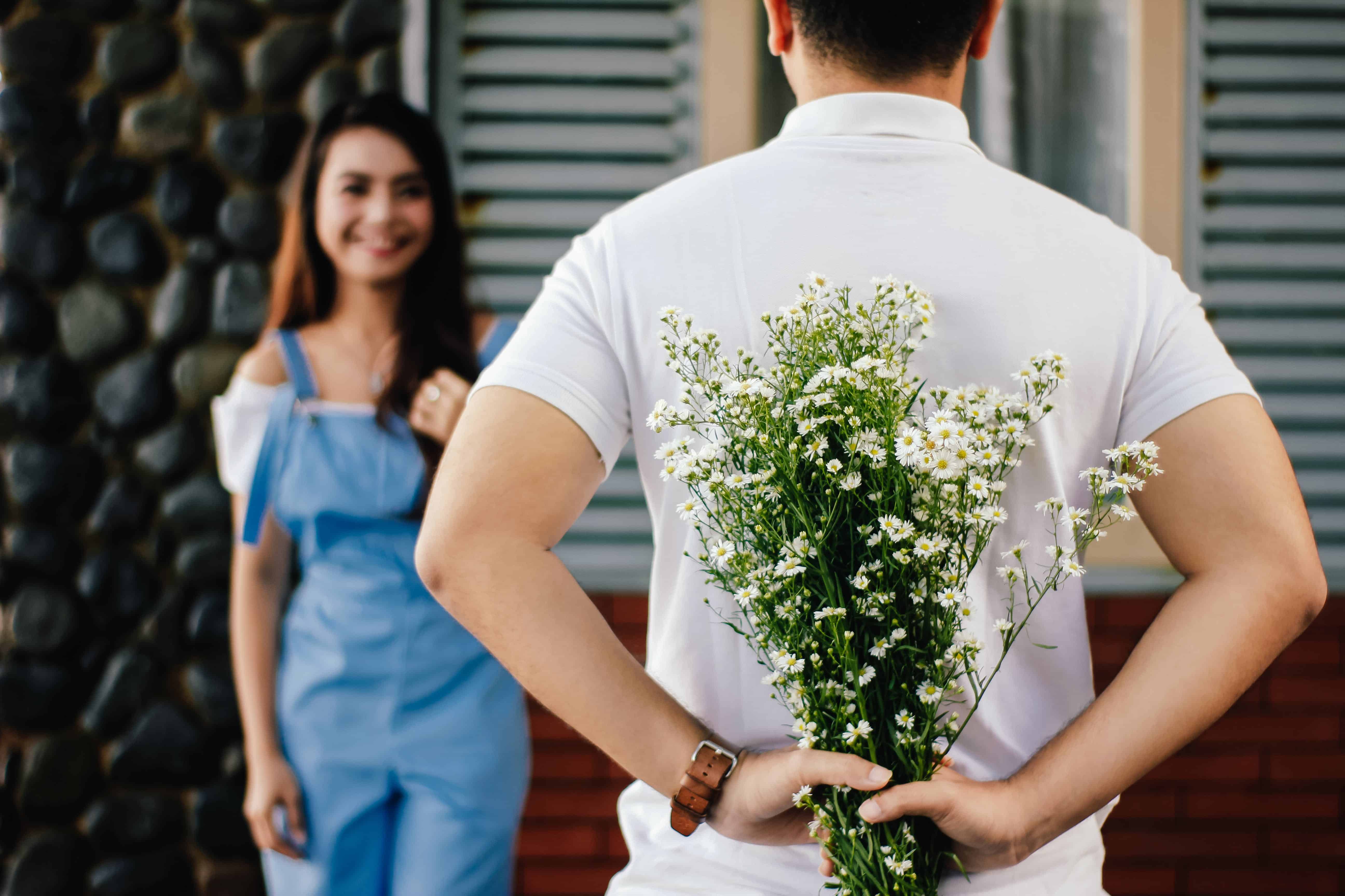 A man hides a bouquet of flowers from his girlfriend behind his back