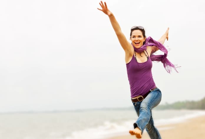 woman-running-happily-along-the-beach-smiling-with-arms-in-the-air