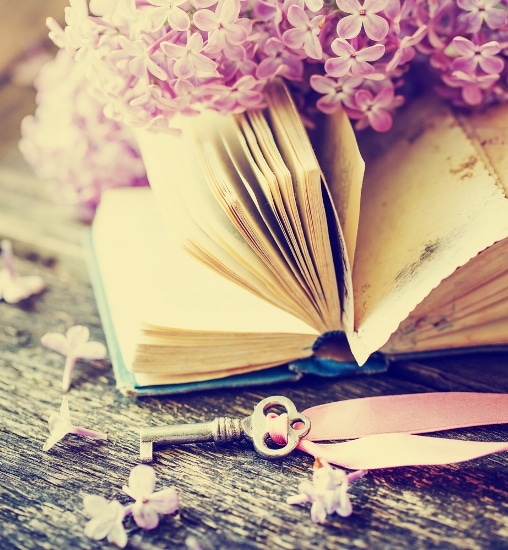 An open book sitting on a wooden table next to a bunch of flowers