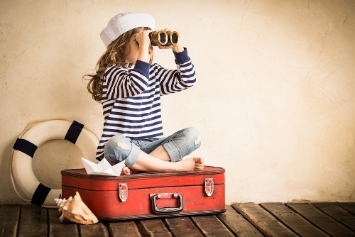 girl sitting on suitcase while looking at binoculars