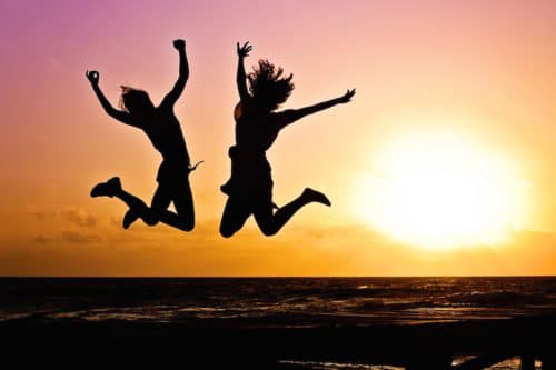 two young people jumping with the sunset on the background