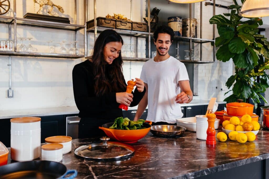 man and woman smiling while cooking together