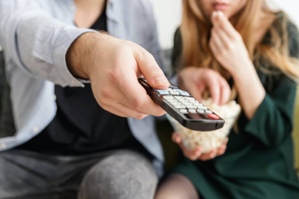 Two people watching TV with remote pointed forward