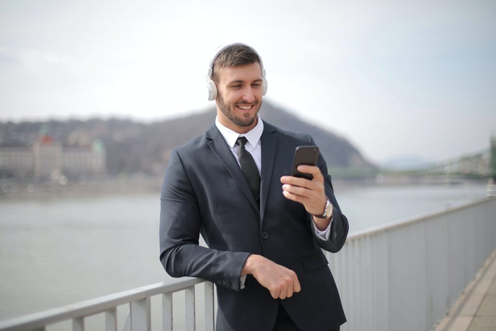 man-in-business-attire-with-white-headphones-and-smiling-at-smartphone