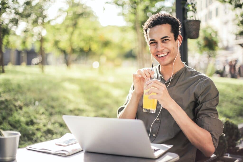 man-smiling-happily-holding-glass-of-juice-and-studying-in-park