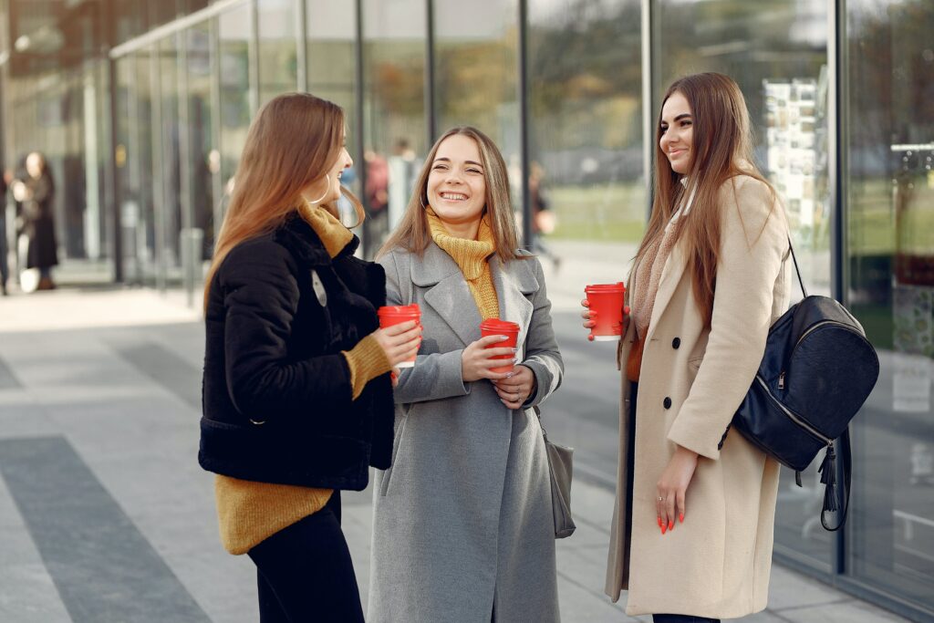 three-women-drinking-coffee-standing-near-a-building-having-a-conversation